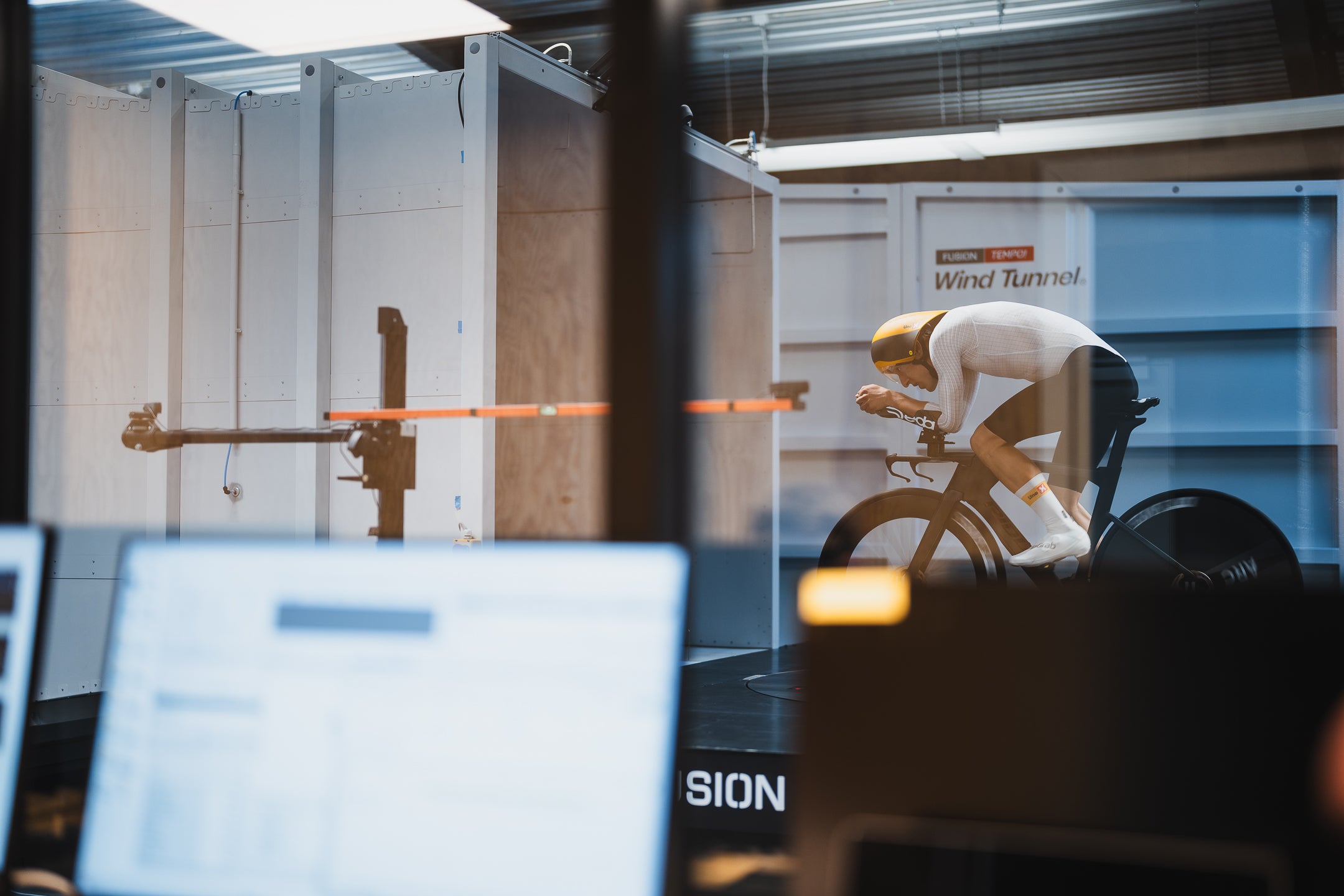 Person on a stationary bike in a wind tunnel with a computer screen in the foreground.